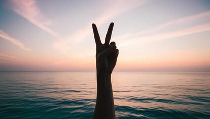 Fototapeta premium Hand Making Peace Sign Over Tranquil Ocean at Sunset 
