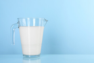 Jug of fresh milk on light blue background, space for text