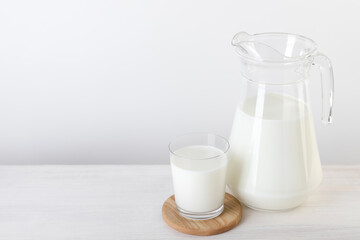 Jug and glass of fresh milk on wooden table, space for text