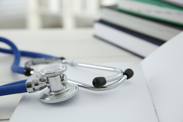 One new medical stethoscope and books on white table, closeup