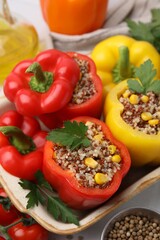 Quinoa stuffed bell peppers in baking dish, parsley, tomatoes and peppercorns on white table, closeup