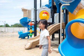 A young girl is sitting on a sky blue slide, smiling and waving. Concept of joy and excitement, as the girl is enjoying her time at the playground