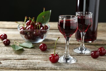 Bottle and glasses of delicious cherry liqueur with juicy berries on wooden table
