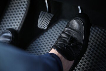 Man in black shoes pushing on pedal of car brake, closeup