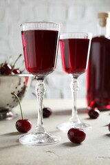 Delicious cherry liqueur in glasses and fresh berries on light grey table