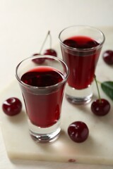 Delicious cherry liqueur in shot glasses and berries on white table, closeup