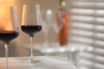 Red wine in glasses on white table against blurred background, space for text