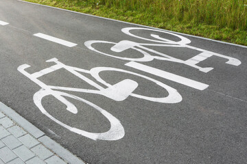 Bicycle path along sidewalk and lawn. Painted bike symbols on asphalt. Urban cycling route. Green space and pedestrian walkway. Ecologically friendly city.