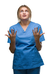 Young caucasian nurse woman wearing surgeon uniform over isolated background crazy and mad shouting and yelling with aggressive expression and arms raised. Frustration concept.