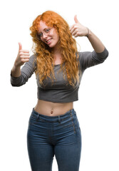 Young redhead woman approving doing positive gesture with hand, thumbs up smiling and happy for success. Looking at the camera, winner gesture.