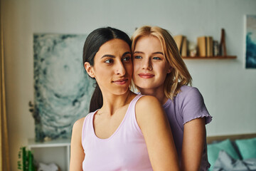 Two women, one with blonde hair and the other with dark hair, are hugging each other with smiles.