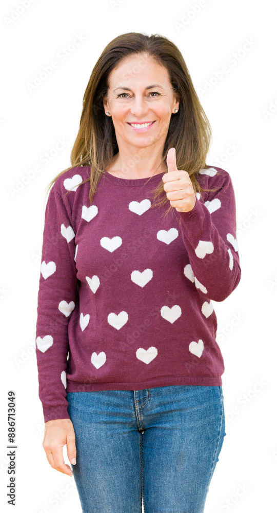 Wall mural beautiful middle age woman wearing hearts sweater over isolated background doing happy thumbs up ges