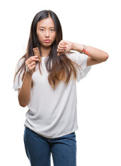 Young asian woman eating chocolate energetic bar over isolated background with angry face, negative sign showing dislike with thumbs down, rejection concept