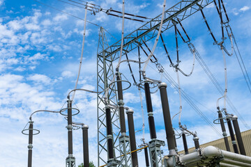 A large electrical power transmission station with numerous towers and wires against a bright blue...