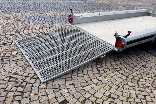 An auto trailer is depicted with its ramp fully lowered, prepared for easy loading and unloading of vehicles. The trailer's robust design and convenient access highlight its suitability for