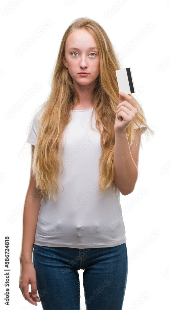 Wall mural Blonde teenager woman holding credit card with a confident expression on smart face thinking serious