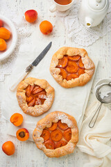 Apricot galette. Homemade three small apricot pie with fresh apricot served for summer tea party on old wooden light table background. Traditional family recipe. Top view with copy space.