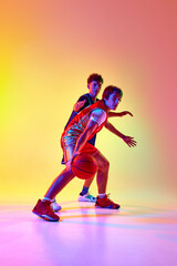 Two basketball players practice with intensity, showcasing their skill and commitment to game in neon light against gradient studio background. Concept of professional sport, match, team games. Ad