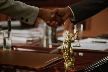 Blindfolded bronze statuette of justice goddess with scales and sword standing on table while two...