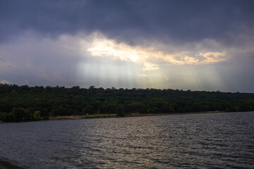 Fototapeta premium The sun's rays are reflected in the water from the river coming out from behind the rain clouds