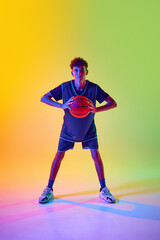 Basketball player in blue sporty uniform, holding ball, posing in neon light against gradient...