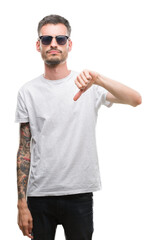 Young tattooed adult man wearing sunglasses with angry face, negative sign showing dislike with thumbs down, rejection concept