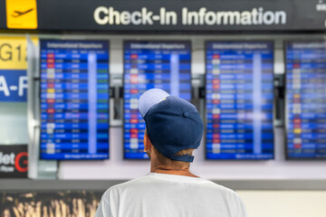 Man traveler checking flight information on digital board at an airport, preparing for his journey. Back view of male tourist in airport terminal looks at airplane schedule board