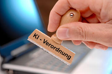 Ein Holzstempel ist beschriftet mit dem Aufdruck KI-Verordnung