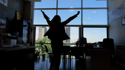 Silhouette of person with raised arms in office moment of triumph and success career achievement. Person silhouette with arms raised high in office signifies victorious moment of success career.