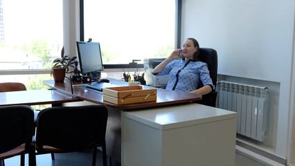 Modern businesswoman seated in corporate office engaged in telephone call for negotiations. In office mid adult female talks on phone conducting important negotiations modern women in workplace.