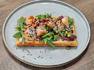 Photo of a Belgian waffle with chicken, corn, bell pepper, lettuce mix and cheese. Belgian waffle with arugula, cream sauce and chicken. Close-up of waffles with different fillings on a light plate