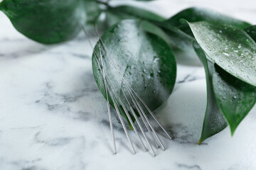 Acupuncture needles and wet green leaves on white marble table, closeup. Space for text