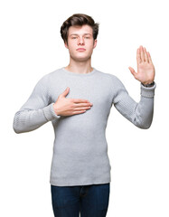 Young handsome man wearing winter sweater over isolated background Swearing with hand on chest and...