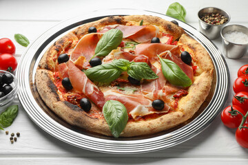 Tasty pizza with cured ham, olives, tomatoes and basil on white wooden table, closeup