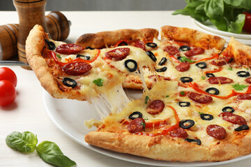 Taking piece of tasty pizza with smoked sausages, olives, pepper and parsley at light wooden table, closeup