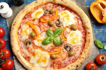 Delicious vegetarian pizza and ingredients on blue wooden table, top view