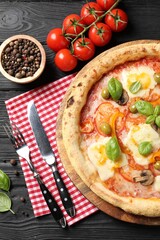 Delicious vegetarian pizza served on black wooden table, top view