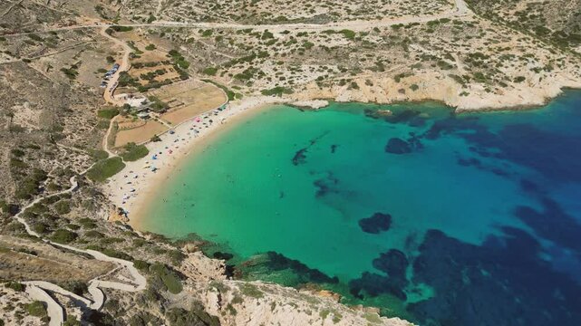 A breathtaking aerial view of Kedros Beach on Donousa Island in the Cyclades, Greece. Turquoise waters lap the shore, surrounded by rocky cliffs and verdant vegetation.