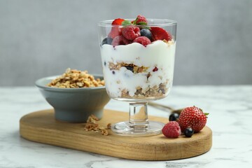 Tasty yogurt with fresh berries and granola in glass dessert bowl on white marble table, closeup