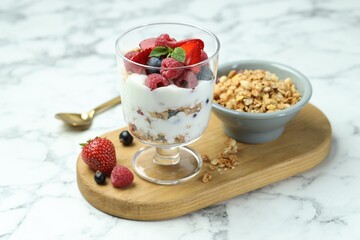 Tasty yogurt with fresh berries and granola in glass dessert bowl on white marble table