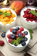 Tasty yogurt with fresh berries, fruits and mint in glasses on table, closeup