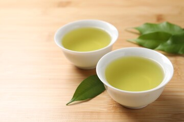 Refreshing green tea in cups and leaves on wooden table, closeup
