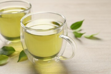 Refreshing green tea in cups and leaves on wooden table, closeup