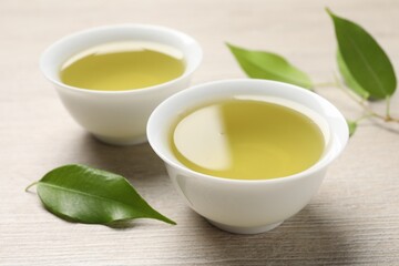 Refreshing green tea in cups and leaves on wooden table, closeup