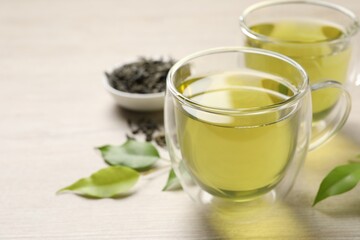 Refreshing green tea in cups and leaves on wooden table, closeup