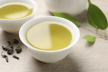 Refreshing green tea in cups and leaves on wooden table, closeup