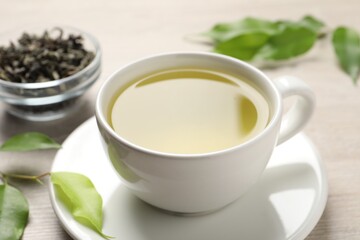 Refreshing green tea in cup and leaves on wooden table, closeup