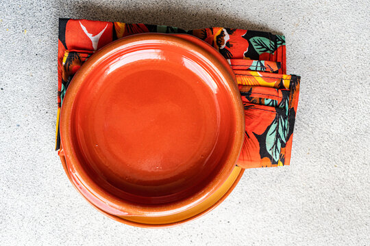 Overhead view of rustic terracotta dinnerware with a colourful napkin