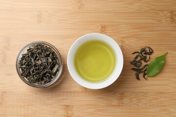 Refreshing green tea in cup and leaves on wooden table, flat lay