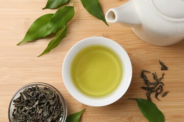 Refreshing green tea in cup, teapot and leaves on wooden table, flat lay